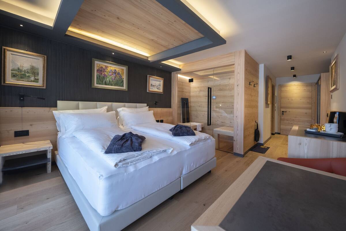 A modern hotel room with a large bed, wooden ceiling, and artwork on the walls.