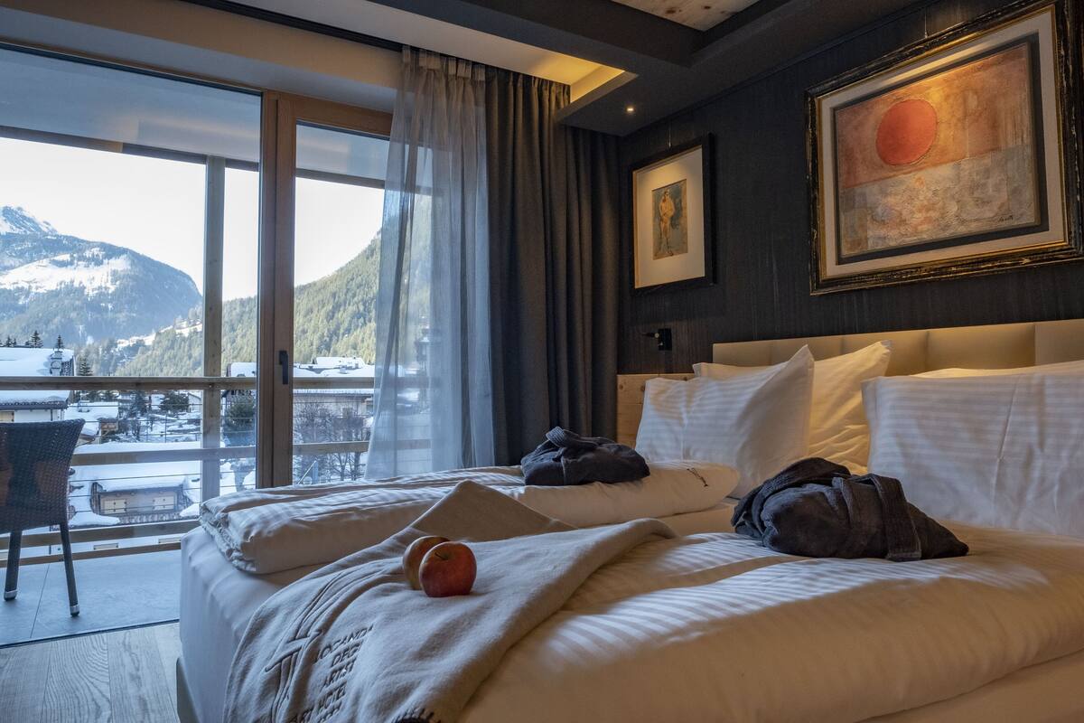 A hotel room with a large bed, a view of mountains, and a painting on the wall.