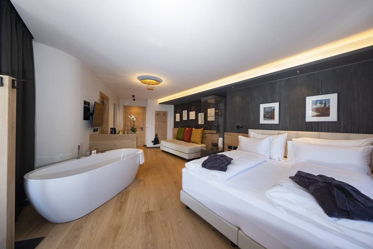 A modern hotel room with a large bathtub, a bed with white linens, and a sofa.