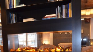 A modern living room with a fireplace, leather armchair, and a bookshelf filled with books. - Art Hotel Locanda degli Artisti (Canazei)