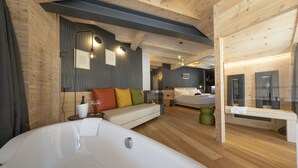 A modern hotel room with a large bathtub, a sofa with colorful cushions, a fireplace, and a separate bedroom area. - Art Hotel Locanda degli Artisti (Canazei)