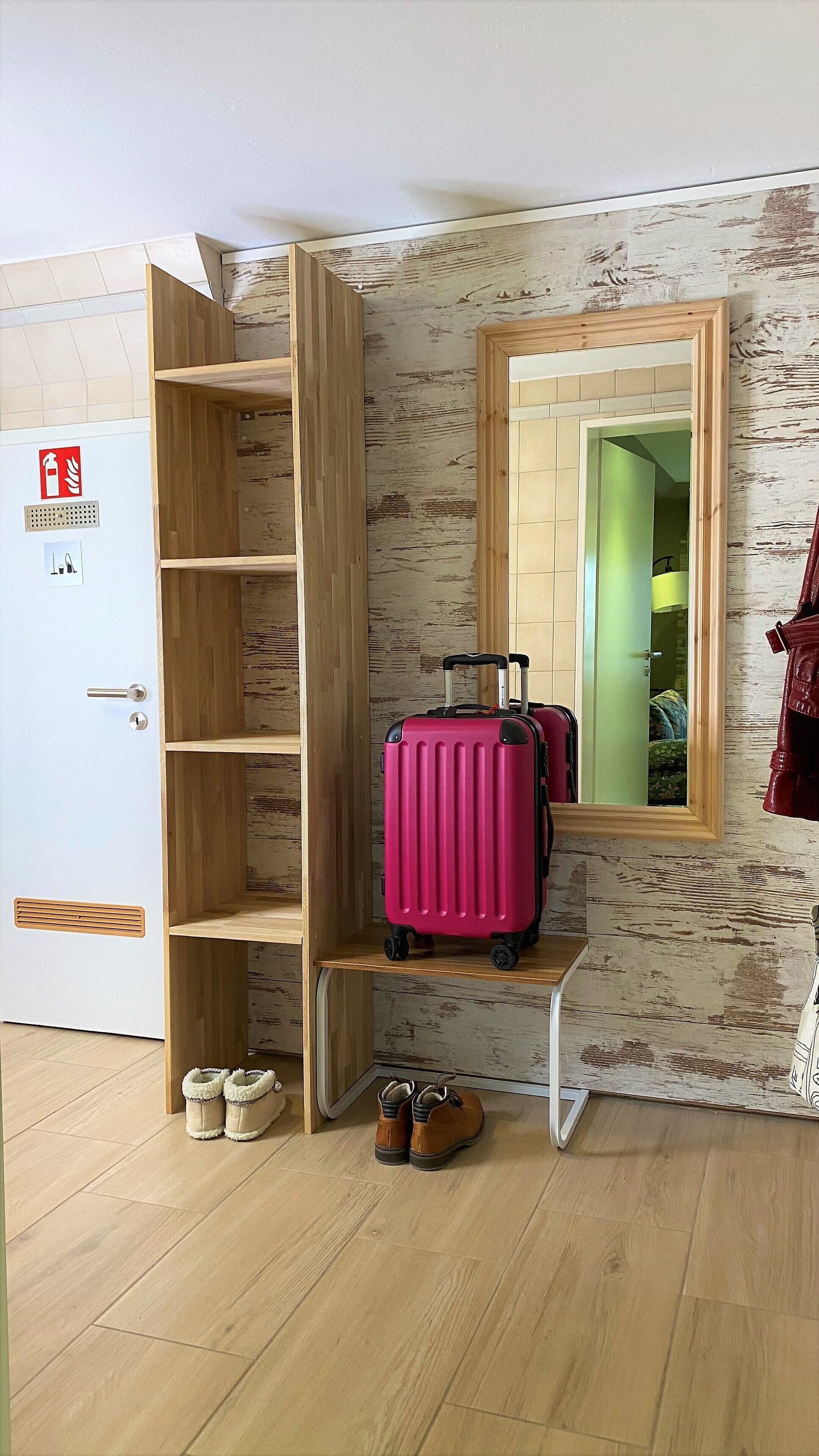 Una habitación con un armario de madera, un espejo y una maleta rosa sobre una estantería.