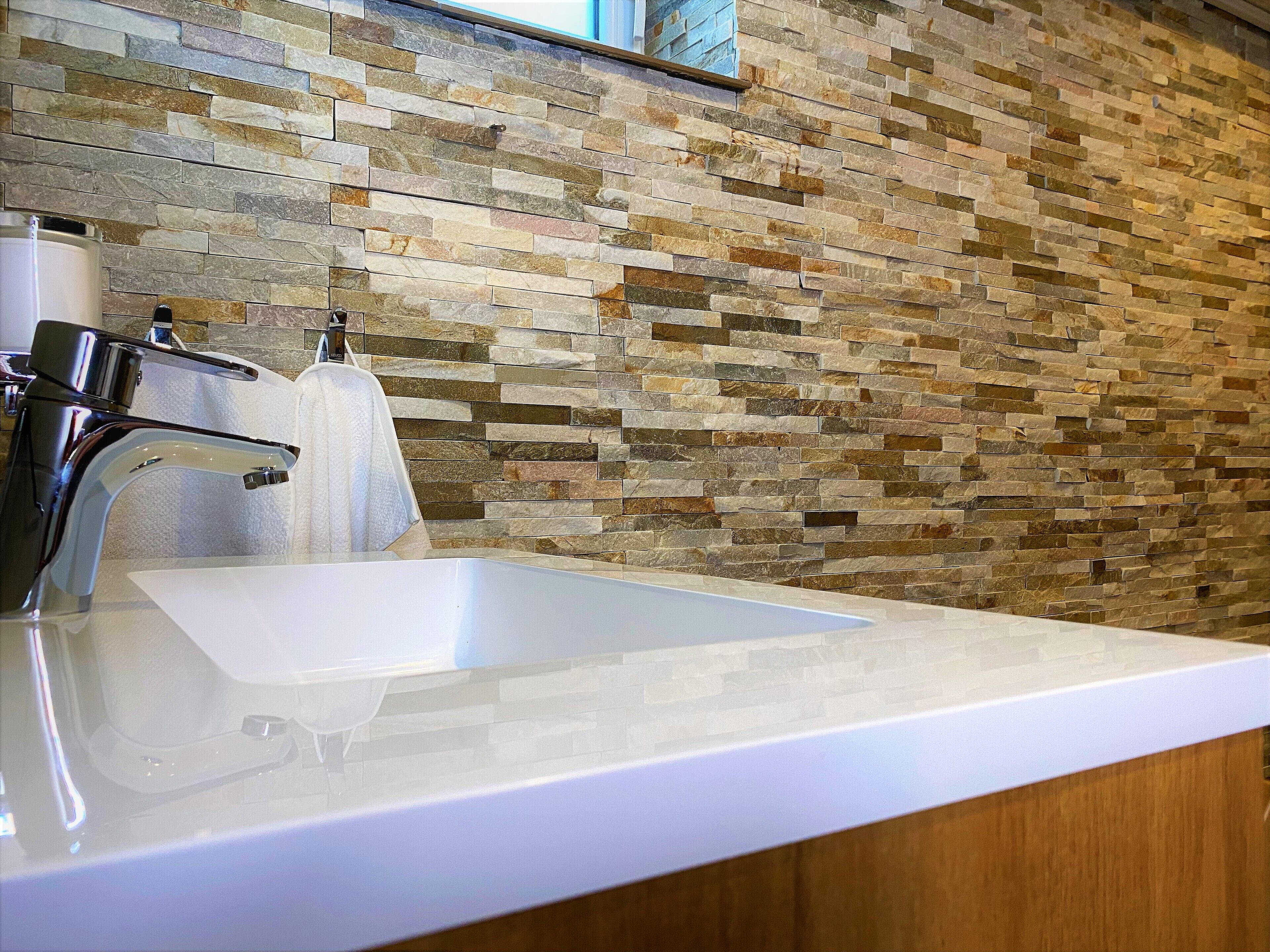 A bathroom with a white sink, chrome faucet, and a stone mosaic wall.