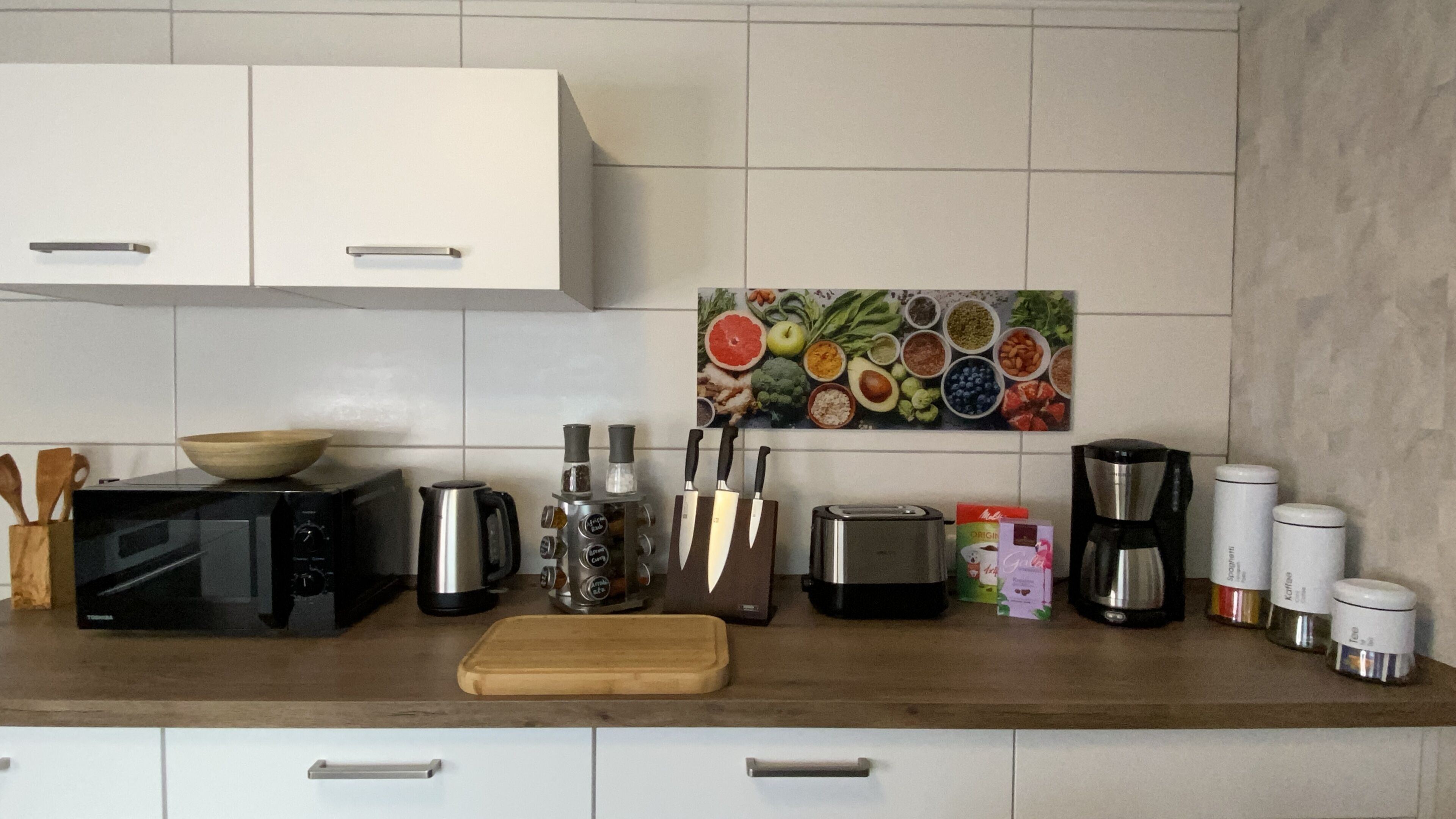A kitchen with white cabinets, a microwave, a toaster, a coffee maker, and various kitchen utensils.