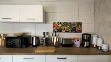A kitchen with white cabinets, a microwave, a toaster, a coffee maker, and various kitchen utensils.