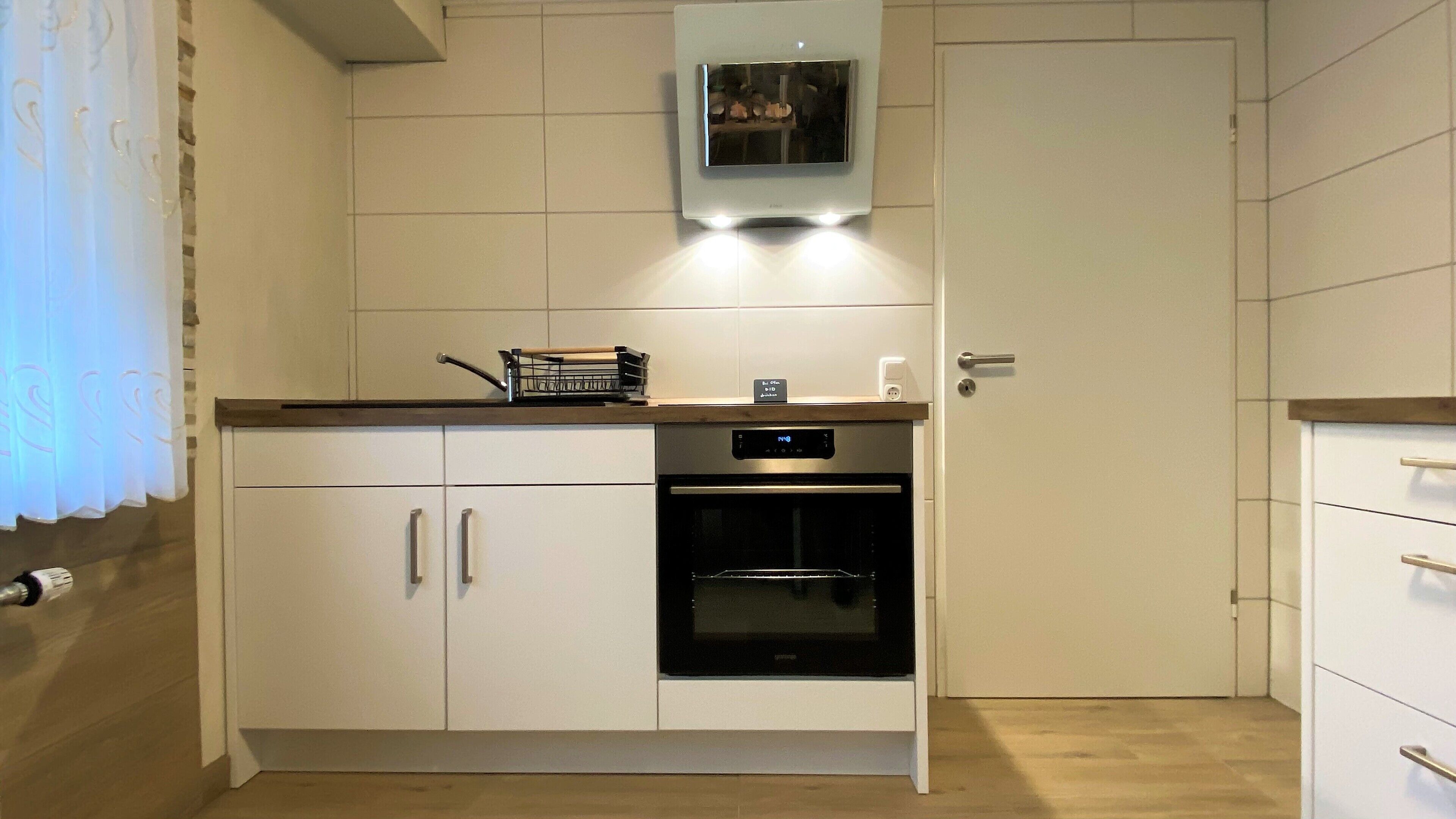Eine moderne Küche mit weißen Schränken, einem eingebauten Backofen und einer kleinen Arbeitsplatte mit Wasserkocher und Kaffeemaschine.