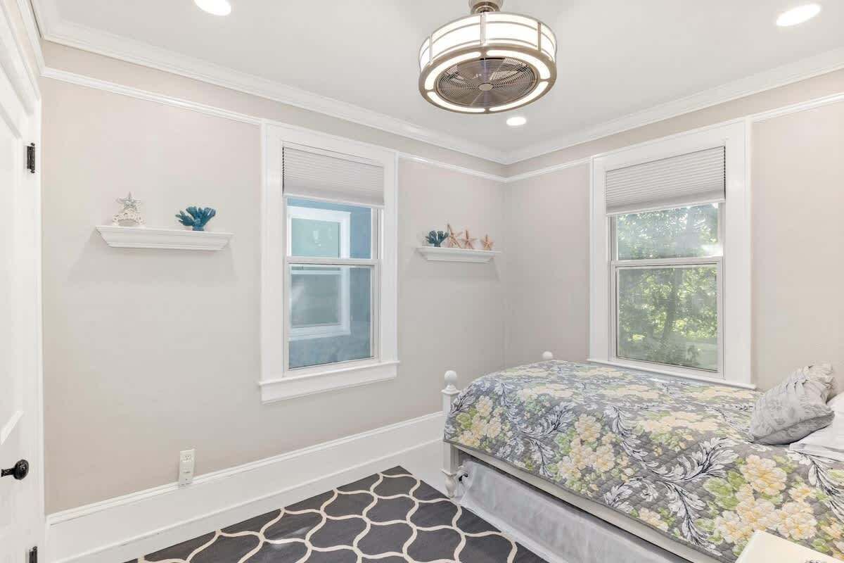 A bedroom with a bed, two windows, a ceiling fan, and a patterned rug.