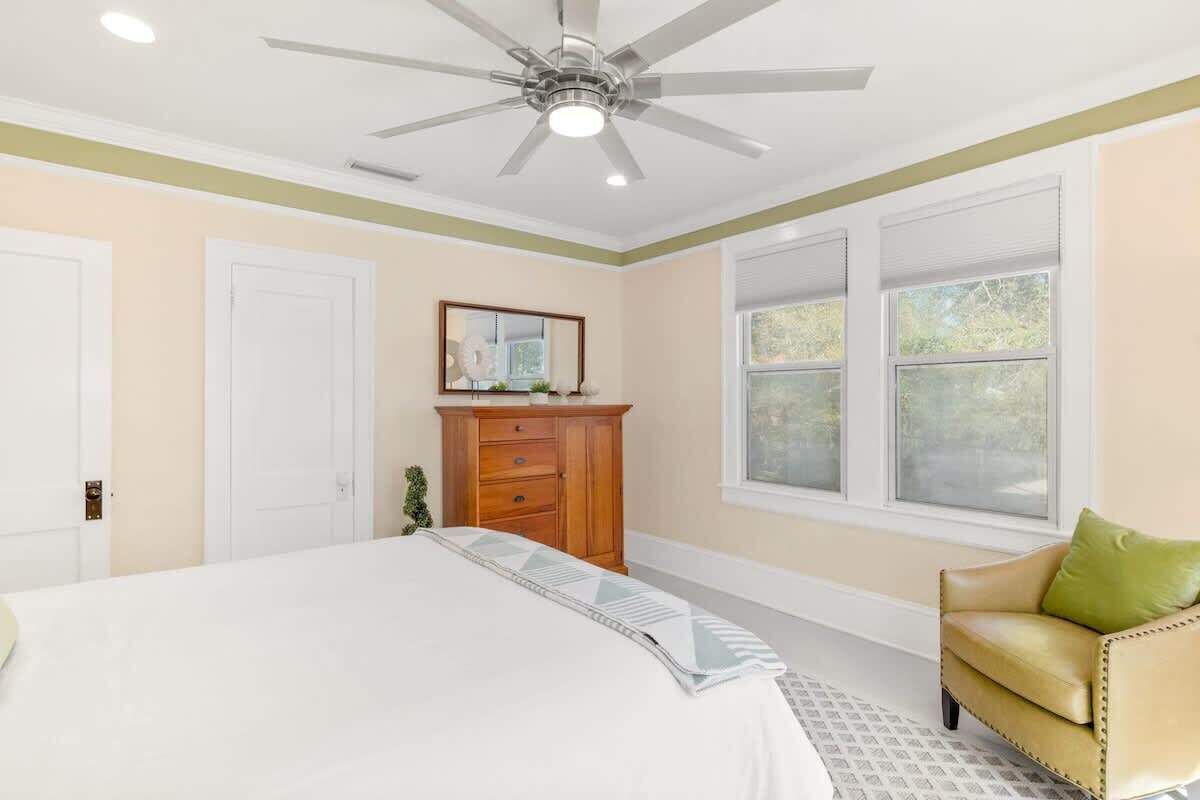 A bedroom with a bed, a wooden dresser, a chair, and a ceiling fan.