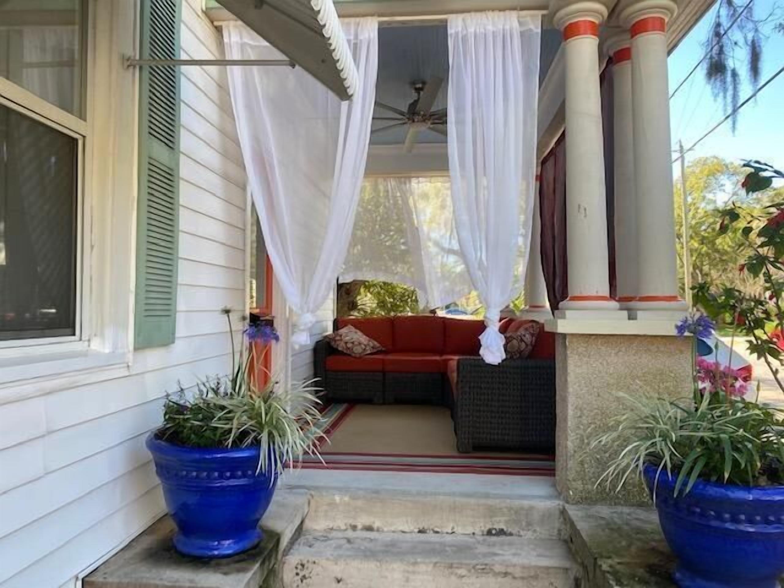 A covered porch with a red sofa, white curtains, and two large blue planters.