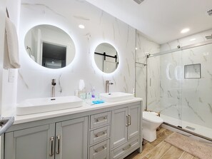 Une salle de bain moderne avec deux lavabos, des toilettes et une douche à parois de verre.