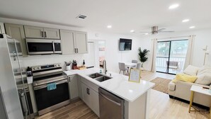 Une cuisine moderne équipée d’appareils électroménagers en acier inoxydable, un coin repas avec une table et des chaises blanches, et un balcon avec vue.