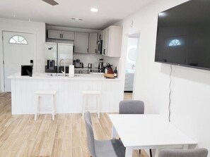A modern kitchen with white cabinetry, a central island with stools, and a dining area with a table and chairs.