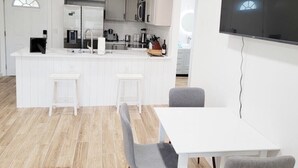Une cuisine moderne avec des meubles blancs, un îlot central doté de tabourets de bar et un téléviseur à écran plat fixé au mur.