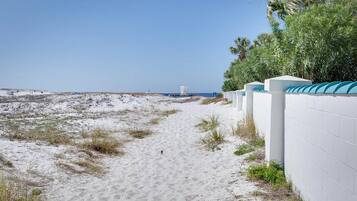 Een zandpad langs het strand dat naar de oceaan leidt, met een witte muur en begroeiing aan de zijkant.