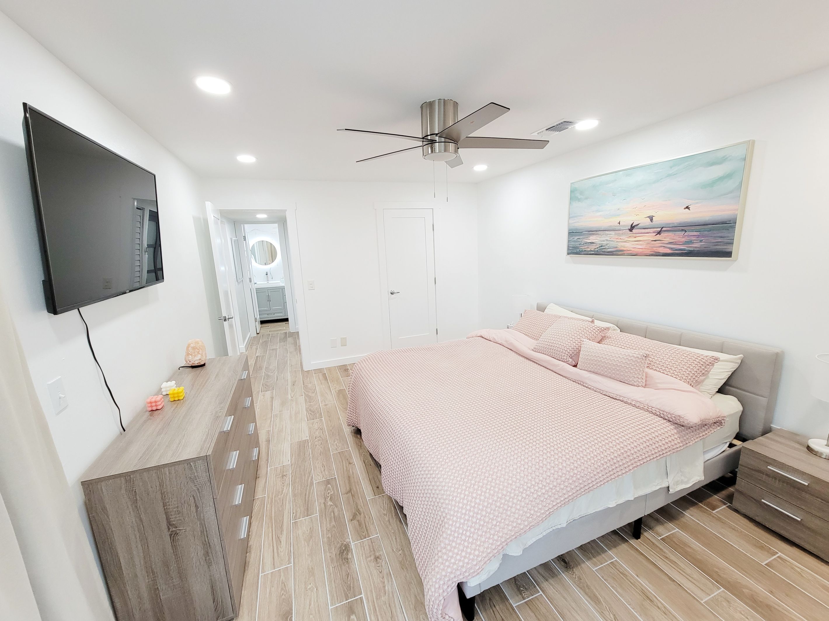 Een moderne slaapkamer met een bed, een plafondventilator, een aan de muur bevestigde televisie en een schilderij boven het bed.