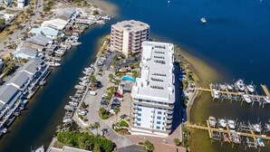 Une vue aérienne d’une marina où sont amarrés de nombreux bateaux, d’un grand immeuble doté de balcons et d’un pont en arrière-plan.