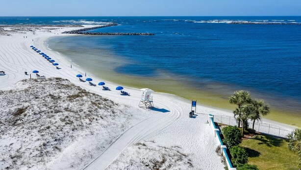 Une plage bordée d’une rangée de parasols bleus, avec une tour de surveillance et une vue dégagée sur l’océan.