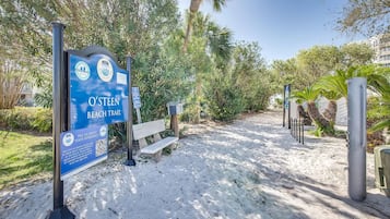 Wandelpad bij het strand met een bord met QR-code voor feedback, een bankje en een zandpad met bomen.
