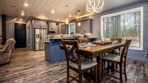 A modern kitchen with a central island, wooden dining table, and chairs. - Dawn's Early Peak - Modern cabin w/ birds-eye view (Smithville)