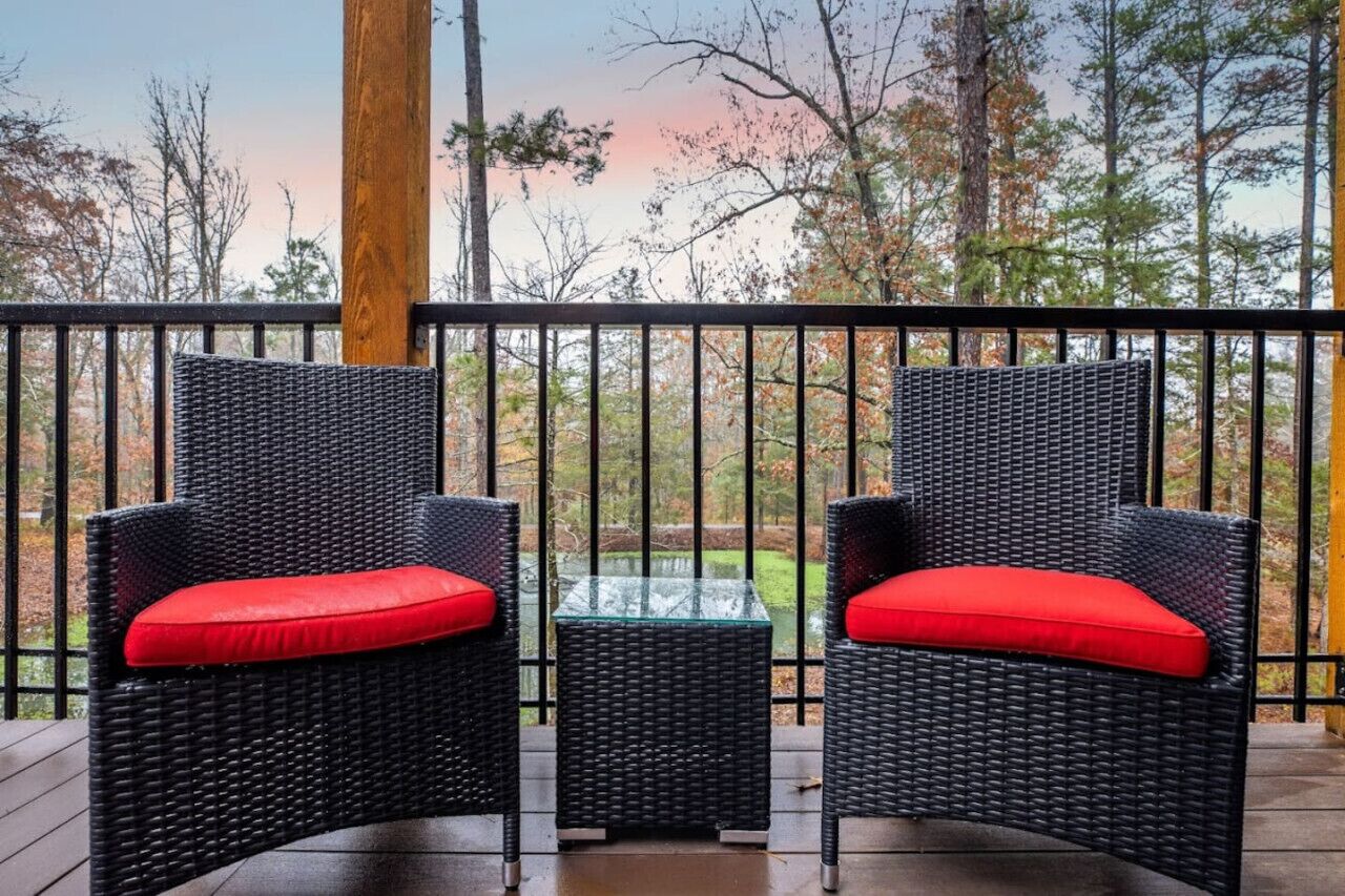 A balcony with two wicker chairs and a glass table, overlooking a forested area.