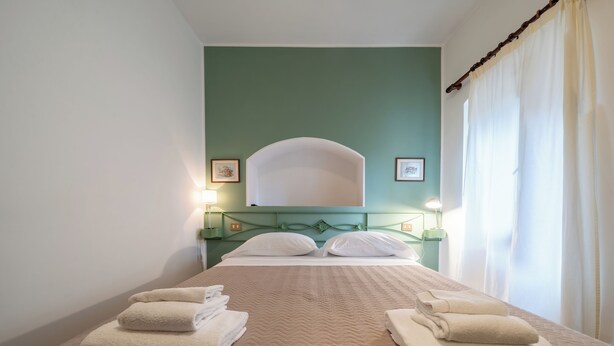 Een netjes opgemaakt bed met een beige sprei, twee kussens en twee opgevouwen handdoeken.