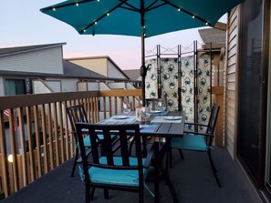 Un balcon avec une table dressée pour deux personnes, des chaises et un grand parasol.