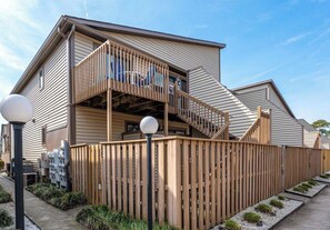 Un bâtiment moderne doté d’une terrasse en bois et d’un escalier menant à un balcon.