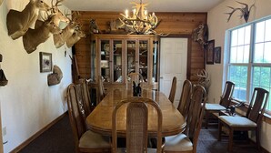 Une salle à manger avec une table et des chaises en bois, entourée de têtes d’animaux empaillées et d’un lustre.