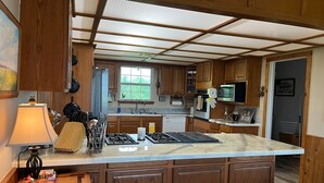 Une cuisine avec des meubles de rangement en bois, un îlot central, une cuisinière, un four à micro-ondes et un évier.