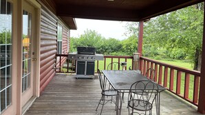 Une terrasse extérieure couverte, équipée d’un barbecue et de chaises en métal.