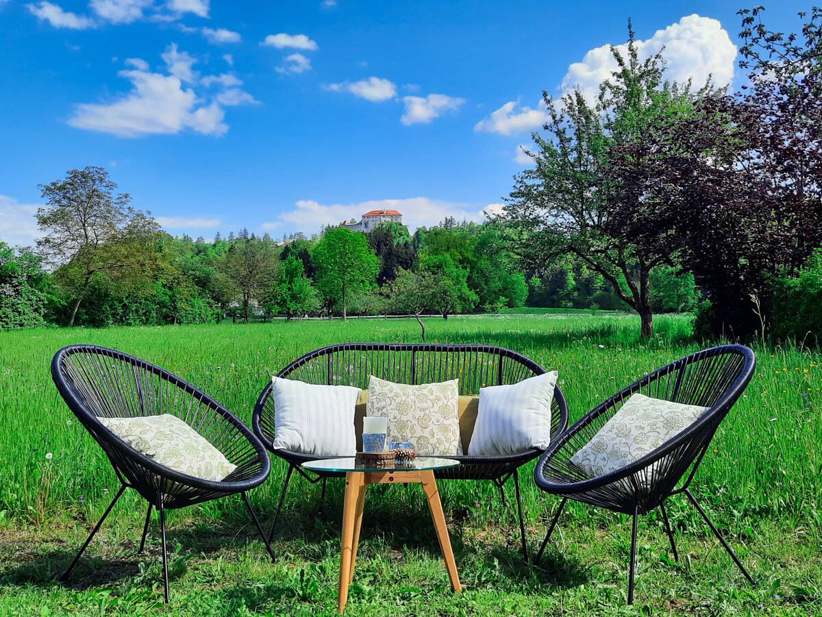 Una silla de mimbre ubicada en un campo verde exuberante con una vista despejada de un edificio lejano.