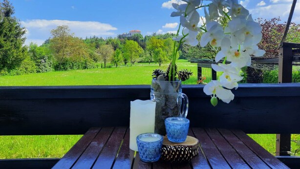 A wooden bench with a vase of white flowers, a candle, and two small blue cups on a wooden table. - Deerwood-Holiday Cozy Apartment with Bled Castle View and Pretty Garden (Bled)