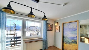 A room with a large window, a radiator, a painting, and a ceiling light fixture. - Deerwood-Holiday Cozy Apartment with Bled Castle View and Pretty Garden (Bled)