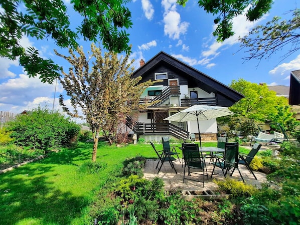 Une maison à deux étages dotée d’un balcon, entourée d’un jardin bien entretenu et agrémentée de mobilier de jardin.
