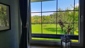 A room with a large window offering a view of a green field and trees. - Deerwood-Holiday Cozy Apartment with Bled Castle View and Pretty Garden (Bled)
