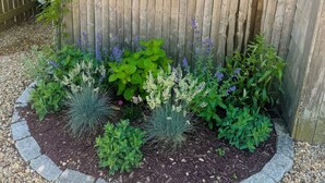 Un parterre fleuri avec différentes plantes et une clôture en bois.