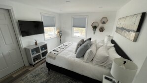 Une chambre à coucher comprenant un lit, une table de chevet, une lampe, une télévision, des fenêtres et une étagère avec des objets décoratifs.