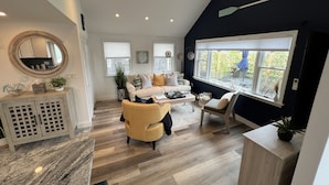 Un salon moderne avec un canapé, des fauteuils et une table basse. Une grande fenêtre offre une vue sur la verdure à l’extérieur.