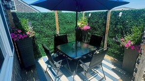 Une terrasse extérieure couverte, dotée d’une table et de chaises, entourée de verdure et agrémentée d’une plateforme en bois.