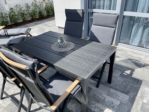 An outdoor patio with a table and chairs, a glass-top table, and a glass vase with decorative stones.