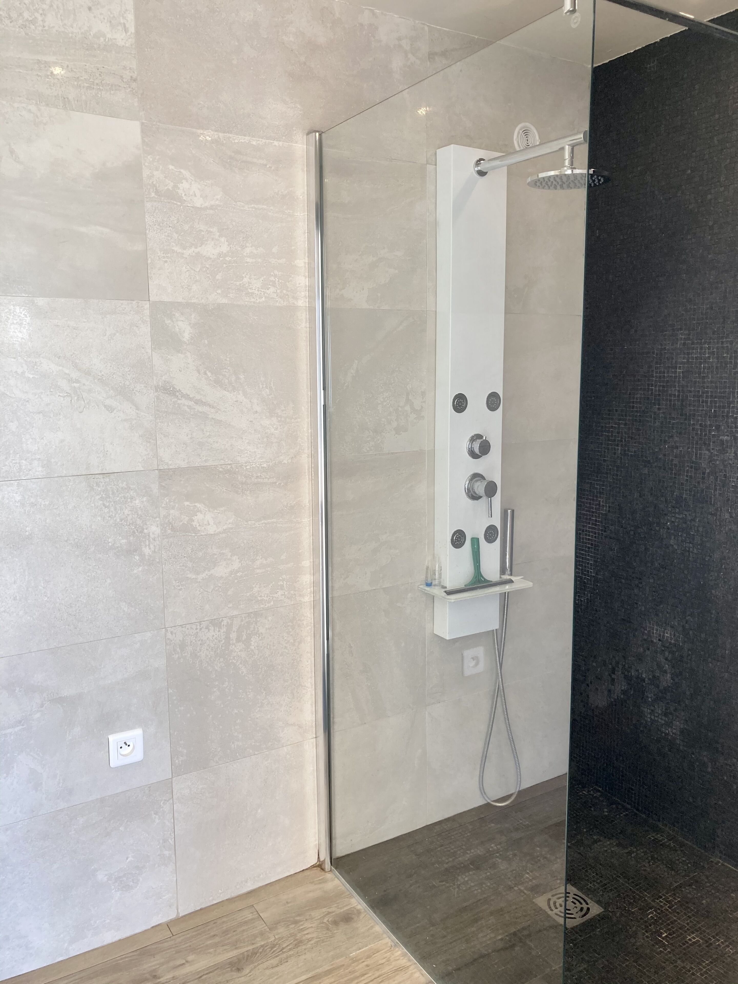 Et moderne brusebad med glasvægge, et kontrolpanel og en mørk flisetapet.