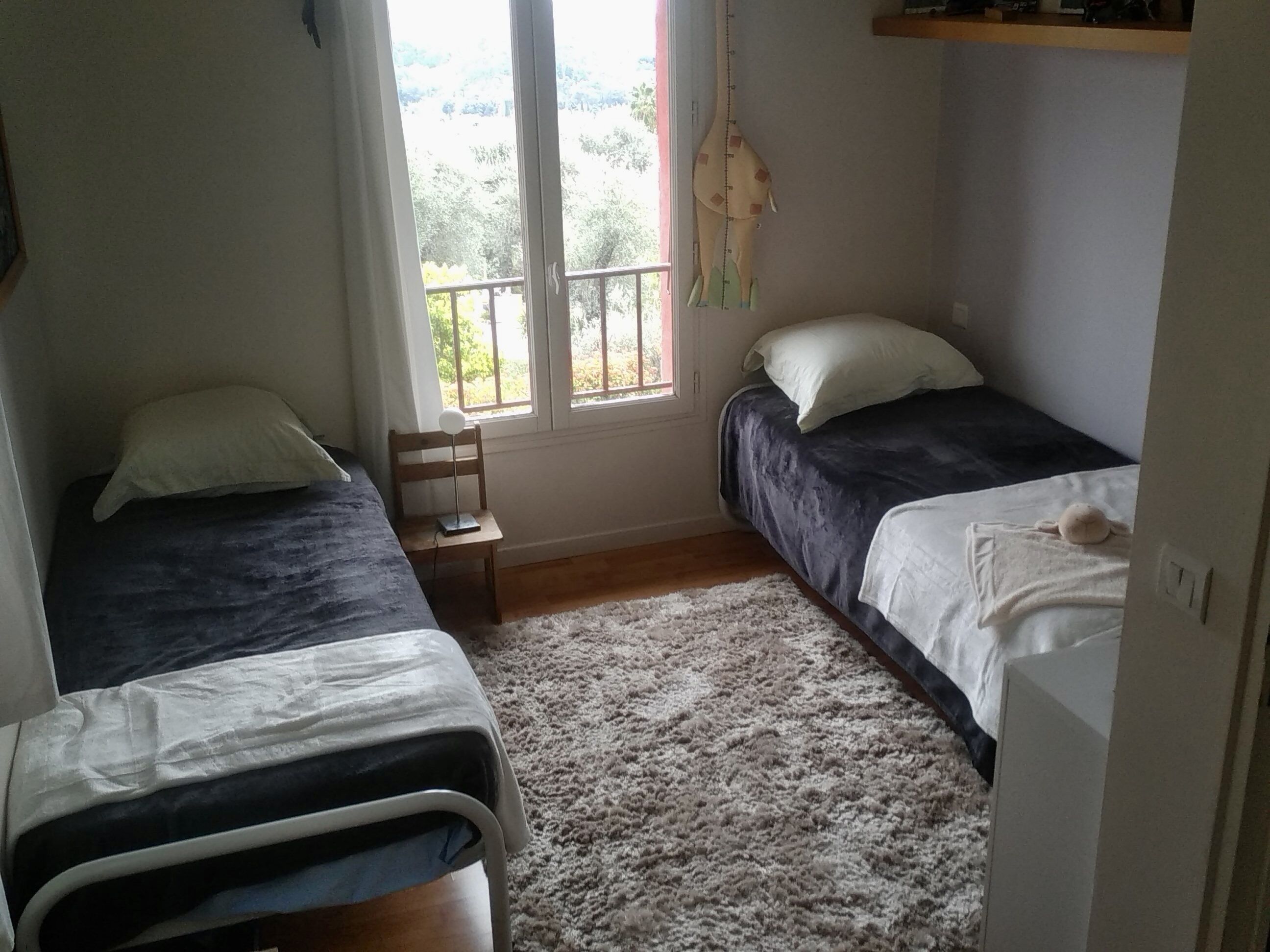 Ein kleines, gemütliches Schlafzimmer mit zwei Betten, einem Nachttisch und einem Fenster mit Blick auf Grünflächen.