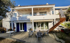 A two-story house with a wooden deck, outdoor seating, and a staircase leading to the upper level.