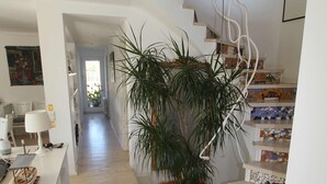 Un intérieur moderne avec un escalier en bois, une plante en pot et un mur blanc orné d’œuvres d’art.