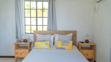 Une chambre avec un grand lit, deux tables de chevet, une fenêtre avec des rideaux et un appareil de climatisation.