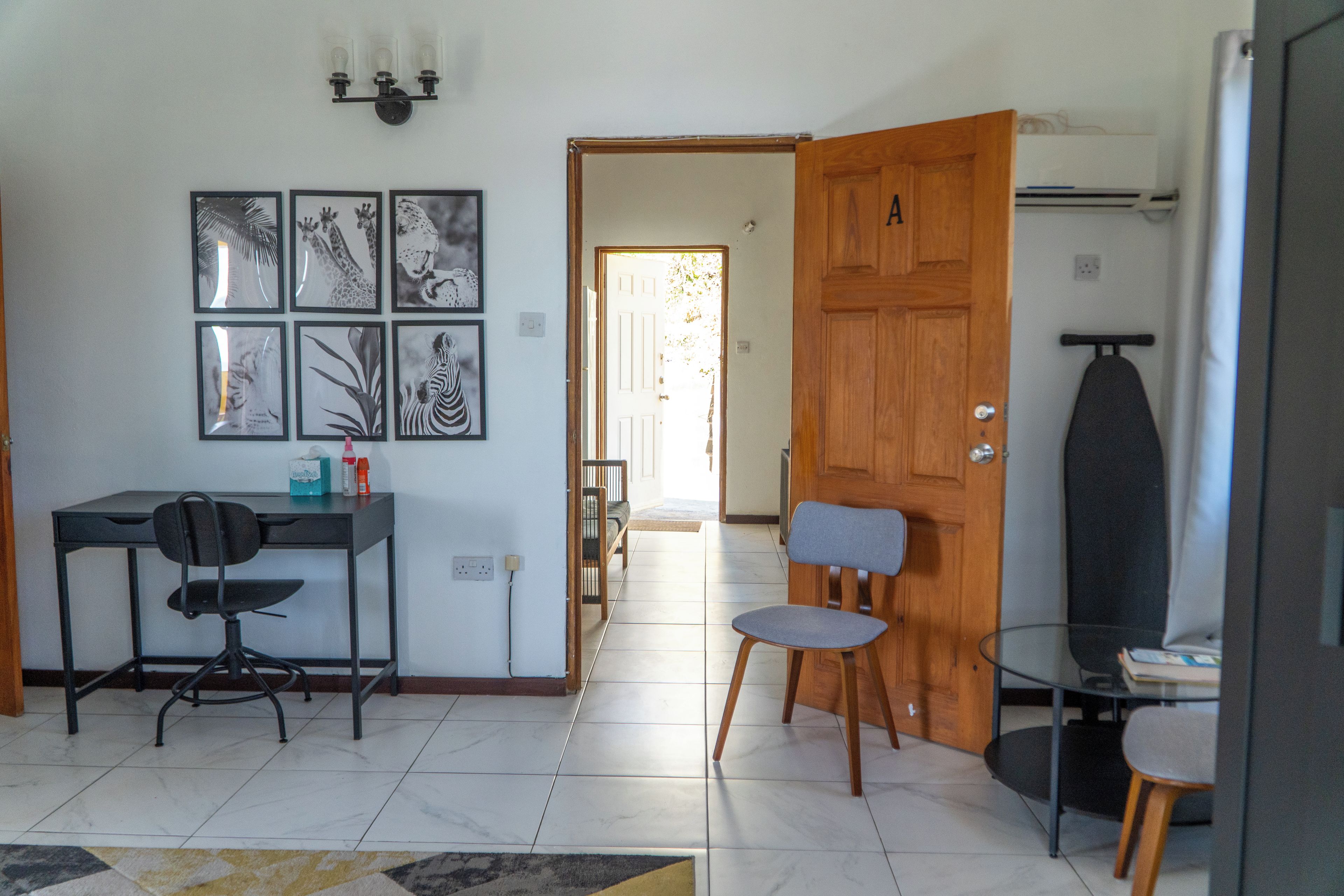 A room with a desk, two chairs, a wooden door, and a wall with framed pictures.