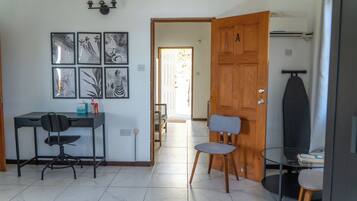 A room with a desk, two chairs, a wooden door, and a wall with framed pictures.