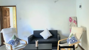 Een woonkamer met een zwarte bank, twee fauteuils met gestreepte kussens, een klein zwart tafeltje en een vaas met gedroogde bloemen.