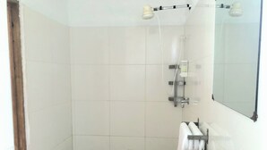 Een kleine, schone badkamer met een wit wastafel, een spiegel en een douche.