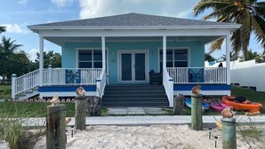 A two-story house with a porch, a staircase, and a sandy beach in front. - Sandy & Salty Beach Cottage (Spanish Wells)
